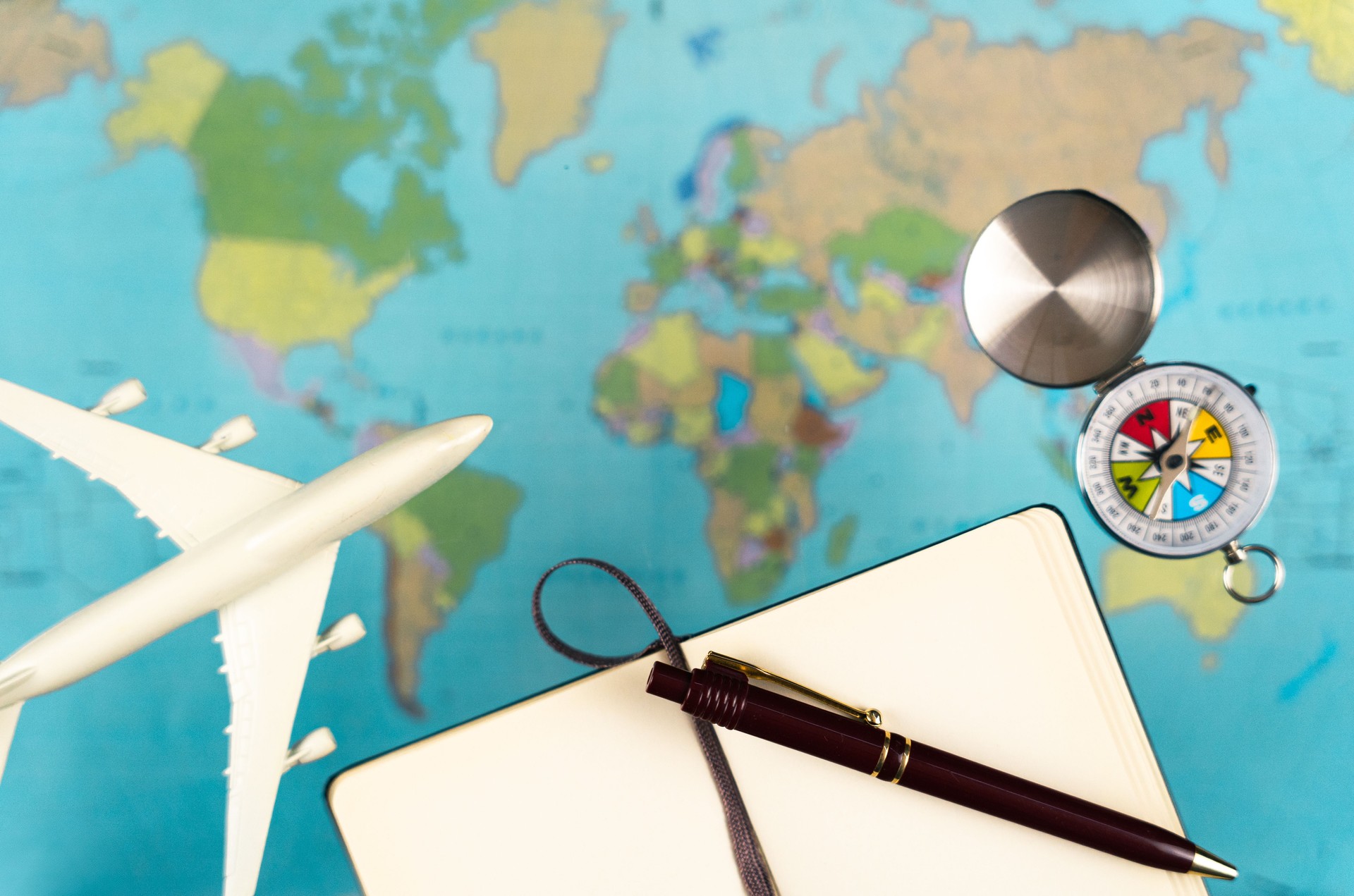 Travel planning featuring world map, airplane, compass, notebook with pen, preparing for upcoming journey