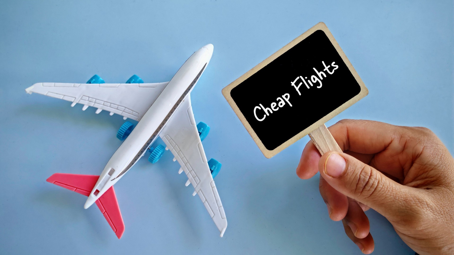 a hand holding notification board written with 'Cheap Flight' with toy airplane beside it.