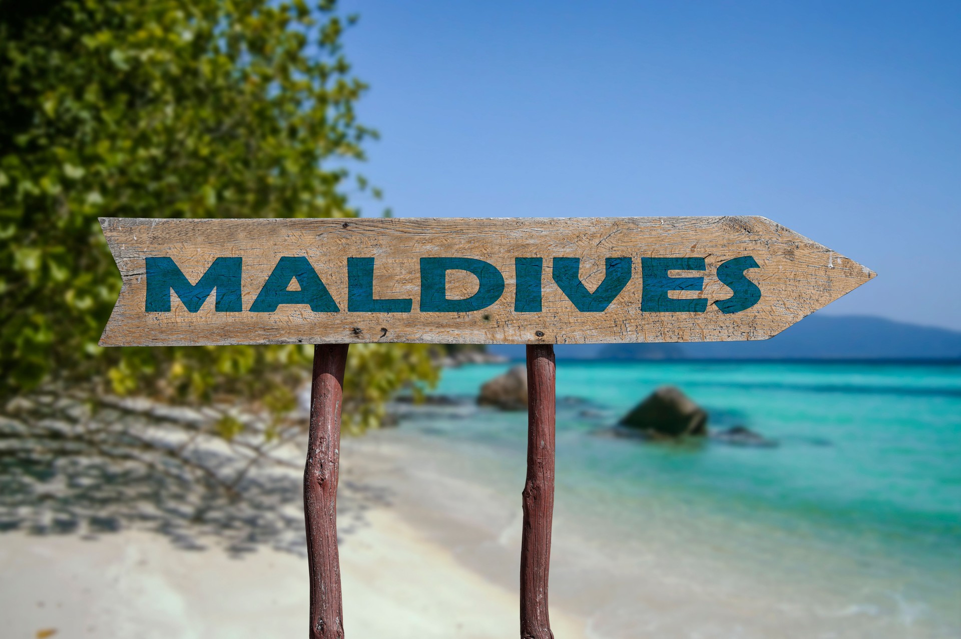 Maldives wooden arrow road sign against tropical beach with white sand and turquoise water background. Travel to Maldives concept.
