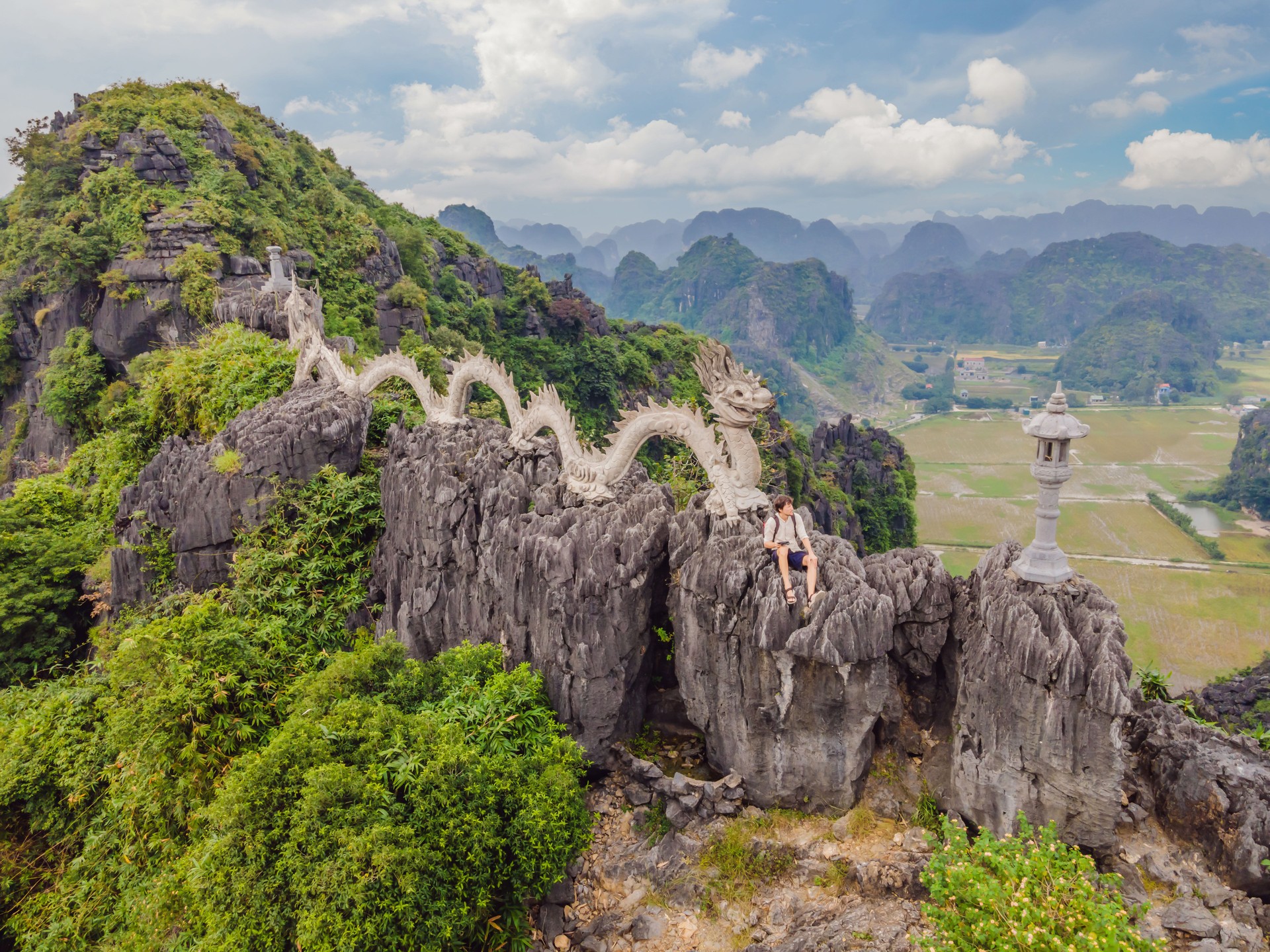 Male tourist on the background of Amazing huge dragon statue at limestone mountain top near Hang Mua view point at foggy morning. Popular tourist attraction at Tam Coc, Ninh Binh. Vietnam travel landscapes and destinations.