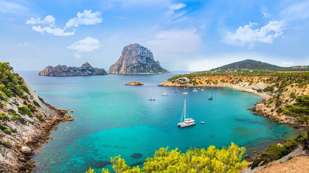 Ibiza beach postcard with flight deal from Dublin. Return direct Ryanair flights from Dublin to Ibiza, Tue 12 May 2026 – Thu 21 May 2026, price €69. Summer travel card design with turquoise sea, sandy beach, sunglasses and travel accessories.